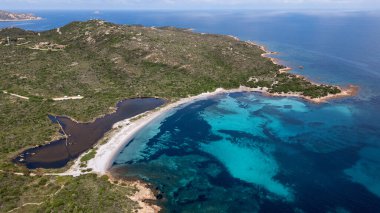 Piscinni sahilinin ve doğal kıyı gölünün çarpıcı panoramik drone görüntüsü. Fotoğraf, güney Sardunya 'nın el değmemiş, el değmemiş güzelliğini, kristal berrak turkuaz suları, beyaz kum ve kıyı boyunca yemyeşil Akdeniz çalılarını yansıtıyor.
