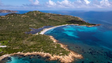 San Teodoro 'daki Baia Salinedda plajının çarpıcı panoramik manzarası. Fotoğraf, kristal berrak turkuaz deniz ile Tavolara Deniz Protokolü 'nün içindeki yemyeşil Akdeniz çalılıklarıyla çevrili doğal göl arasındaki eşsiz kum şeritlerini yakalıyor.