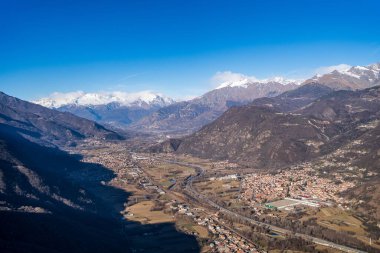 Sacra di San Michele 'den Susa Vadisi' nin geniş hava manzarası. Karla kaplı Cottian Alpleri 'nin panoraması, şehir yerleşimleri ve Fransa sınırına doğru giden A32 karayolu açık mavi kış gökyüzü altında..