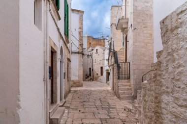 Cisternino 'nun tarihi merkezinde dar bir caddenin manzarası. Beyaz yıkanmış evler, geleneksel taş kaldırımlar ve bulutlu bir gökyüzünün altında Valle d 'Itria' nın tipik mimarisi. Güney İtalya 'daki ortaçağ köyünün otantik bir örneği..