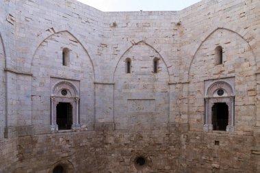 Castel del Monte 'nin sekizgen avlusunun manzarası. Kireçtaşı duvarlarda zarif dekore edilmiş kapılar ve ortaçağ pencereleri var. Frederick II 'nin mimarisinin mükemmel geometrisi ve simetrisi Apulia, İtalya, UNESCO miras alanı.