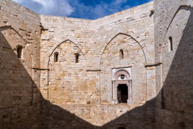 Castel del Monte 'deki (UNESCO) avlunun detayları. Ogival kemer kapılı ve pencereli kireçtaşı duvarlar. Keskin üçgen bir gölge, Frederick II 'nin ortaçağ geometrisini güçlendiriyor. Apulia 'daki heybetli tarihi atmosfer.