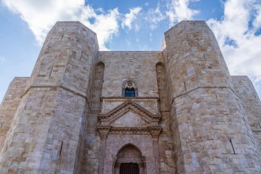 Andria 'daki Castel del Monte' nin ana cephesinin alçak açılı görüntüsü. Heybetli geçit, mavi gökyüzünün altında bulutlu iki devasa sekizgen kireçtaşı kule tarafından çerçevelenmiş. Apulia 'daki Swabian mimarisinin ikonik UNESCO Dünya Mirası sahası.