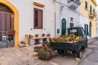 Gelibolu 'nun enfes bir manzarası var. İçinde sulu ve kaktüsler için saksı olarak kullanılan üç tekerlekli küçük bir vintage kamyon var. Tipik Salento mimarisi, arka planda beyaz duvarlar ve sarı aksanlı. Yaratıcı şehir dekorasyonu.