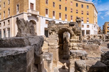 Lecce 'deki Roma amfitiyatro kemerlerine yakın çekim. Fotoğraf, M.Ö. 2. yüzyıl arkeolojik kalıntılarının, İtalya 'nın Puglia kentindeki bulutların dağınık olduğu açık mavi gökyüzünün altındaki Piazza Sant' Oronzo 'daki modern mimariyle zıt düşüşünü gösteriyor..