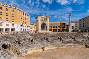 Lecce 's Piazza Sant' Oronzo 'daki Roma Amfitiyatrosu, M.Ö. 2. yüzyıldan kalma. Fotoğraf, şehrin zengin arkeolojik mirasını gözler önüne seren taş katlar, Rönesans Sedile binası ve mavi gökyüzünün altındaki Aziz Orontius Sütununu içeriyor..