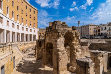 Lecce 'deki Roma amfitiyatro kemerlerine yakın çekim. Fotoğraf, M.Ö. 2. yüzyıl arkeolojik kalıntılarının, İtalya 'nın Puglia kentindeki bulutların dağınık olduğu açık mavi gökyüzünün altındaki Piazza Sant' Oronzo 'daki modern mimariyle zıt düşüşünü gösteriyor..