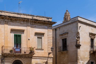 Lecce 'nin Lecce Taşı' ndaki tarihi saraylara kısa bir bakış. Fotoğrafta antik balkonlar, bir fener, bir köşedeki aziz heykeli ve Salento, Puglia, İtalya 'nın göbeğindeki açık mavi gökyüzünün altındaki Barok çan kulesinin tepesi görülüyor..