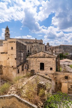 İtalya 'nın Puglia kentindeki Gravina antik köyünün manzarası. Mavi bulutlu gökyüzü altında tarihi kireçtaşı binalarla çevrili, çan kulesi ve kubbesi ile Santa Maria Assunta Katedrali yer almaktadır. Geleneksel Murgia mimarisi.