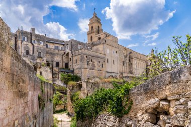 İtalya, Puglia 'daki Gravina Piaggio bölgesinin panoramik manzarası. Ön planda yıkılmış kaya kesimli evler ve bulutlu bir gökyüzünün altındaki tarihi kireçtaşı binaların üzerinde yükselen Katedral çan kulesi. İkonik ve eski Murgia manzarası.