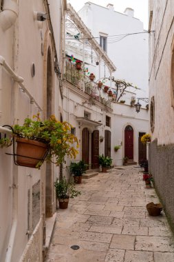Martina Franca 'da beyaz yıkamalı evler, taş kaldırımlar ve bir sürü çiçek saksısı olan tipik bir ara sokak manzarası. Fotoğraf, Itria Vadisi 'nin gösterişli balkonları ve İtalya' nın geleneksel mimarisi ile sakin ve pitoresk atmosferini yakalıyor..