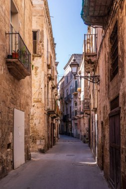 Taranto 'nun Eski Kasabası' ndaki Vico Serafico 'nun anlamlı manzarası. Carparo taşındaki yüksek tarihi binalar, demir balkonlar ve geleneksel sokak lambaları tarihi merkezde otantik ve zamansız bir atmosfer yaratır..