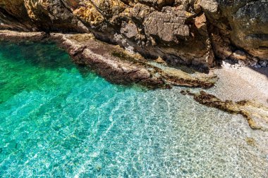 Close-up of the transparent turquoise water at Paternella Cove in Terrasini. The photo shows sun reflections on the rocky seabed and the wild beauty of the Sicilian coast. An untouched natural paradise ideal for travel and tourism.