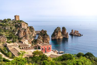 Sicilya 'daki tarihi Tonnara di Scopello' nun panoramik manzarası. Kırmızı bina ve taş yapılar kristal berrak sudan yükselen deniz yığınlarını gözden kaçırıyor. Antik gözetleme kuleleri açık bir gökyüzünün altındaki kayalıklara hükmediyor. İkonik İtalyan kıyı manzarası.