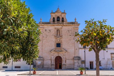 Sicilya, Ispica 'daki Madonna del Carmine Kilisesi' nin ön manzarası. Barok kireç taşı cephesi açık mavi gökyüzünün altındaki yeşil ağaçlar tarafından çerçevelenmiştir. Geçidin üstündeki çan kulesinin ve Bakire Heykeli 'nin detayları. İtalyan mirası sitesi.