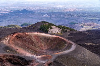 Etna Dağı 'ndaki Silvestri Kraterlerinin hava görüntüsü. Turistler kırmızı ve siyah toprak içeren volkanik koni boyunca yürürler. Arka planda, İtalya 'nın Sicilya kentindeki lav akıntıları, ormanlar ve Catania ovaları arasındaki zıtlık.