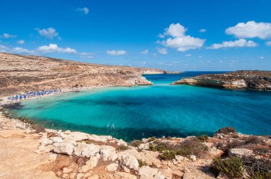 Lampedusa 'daki Rabbit Sahili' nin havadan görüntüsü. Turkuaz berrak sular kireçtaşı kayalıklarıyla çevrili beyaz sahili yıkıyor. Tavşan Adası açık mavi gökyüzünün altında körfezin ortasında duruyor. Akdeniz, İtalya 'da Doğal Cennet.