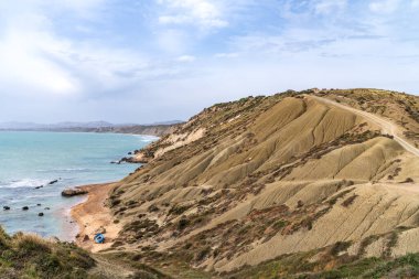 Sicilya, Agrigento 'daki Punta Bianca Doğa Koruma Alanı' nın çarpıcı kıyı manzarası. Görüntü, bulutlu bir gökyüzünün altında küçük mavi bir teknesi ve turkuaz bir denizi olan vahşi bir sahile doğru eğilen karakteristik Marl uçurumlarını gösteriyor. Gerçek bir saklı mücevher..