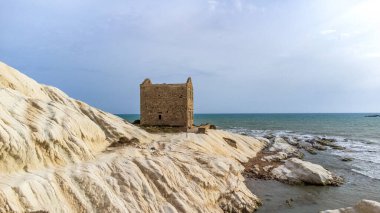 Sicilya 'daki Punta Bianca Rezervi' nin göz kamaştırıcı manzarası. Görüntü, denize bakan beyaz bir mermer kayalıkta izole edilmiş antik Gümrük Dairesi 'ni gösteriyor. Parlak beyaz kaya, taş bina ve mavi deniz arasındaki kontrast benzersizdir ve ikonidir.