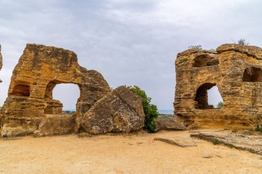 Agrigento 'daki Tapınak Vadisi' nin duvarlarına oyulmuş antik arkozolium mezarları. Kireçtaşı kalıntıları, kemerli açıkları olan, bulutlu bir gökyüzüne karşı durmakta, Sicilya denizine tepeden bakan.