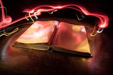 Bir yığın eski kitap. Ahşap masanın üzerinde antika bir kitap. Karanlıkta parlayan bir kitabın etrafında sihirli bir yıldırım. Seçici odak