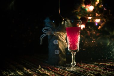 Noel süslemeli bir kadeh şarap. Kırmızı şarap kristal bardakta, renkli halıda şişe ve yaratıcı yeni yıl süslemeleri. Boşluğu kopyala