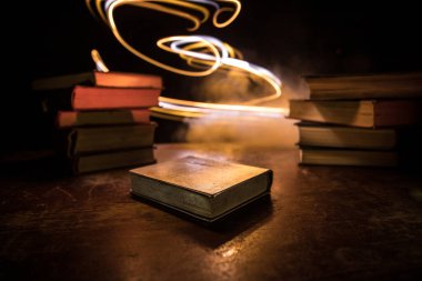 Bir yığın eski kitap. Ahşap masanın üzerinde antika bir kitap. Karanlıkta parlayan bir kitabın etrafında sihirli bir yıldırım. Seçici odak