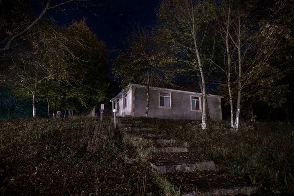 Old house with a Ghost in the forest at night or Abandoned Haunted Horror House. Old mystic building in dead tree forest. Surreal lights. Horror Halloween concept