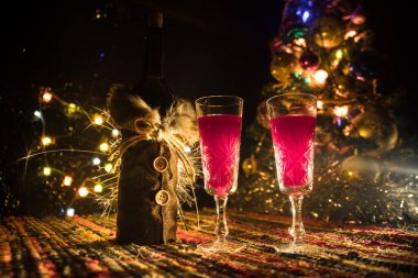 Noel süslemeli bir kadeh şarap. Kırmızı şarap kristal bardakta, renkli halıda şişe ve yaratıcı yeni yıl süslemeleri. Boşluğu kopyala