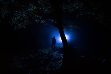 Karanlık ormanda ışıkla duran bir insan silueti. Korku Cadılar Bayramı konsepti. Gecenin karanlığında ürkütücü bir ormanda tuhaf bir siluet.