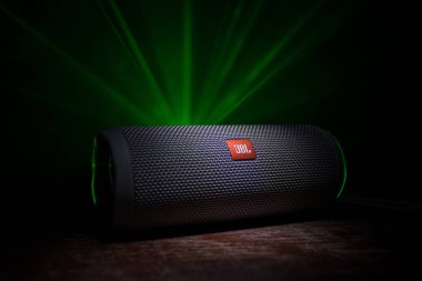 BAKU. AZERBAIJAN - 28.07.2020: JBL Flip 4 Bluetooth Hoparlörü, ahşap masaya yakın çekim, renkli ışıklar ve arka planda sis. Seçici odak