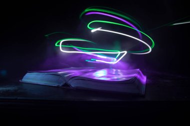 Bir yığın eski kitap. Ahşap masanın üzerinde antika bir kitap. Karanlıkta parlayan bir kitabın etrafında sihirli bir yıldırım. Seçici odak