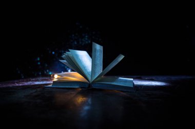 Bir yığın eski kitap. Ahşap masanın üzerinde antika bir kitap. Karanlıkta parlayan bir kitabın etrafında sihirli bir yıldırım. Seçici odak