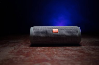 BAKU. AZERBAIJAN - 28.07.2020: JBL Flip 4 Bluetooth Hoparlörü, ahşap masaya yakın çekim, renkli ışıklar ve arka planda sis. Seçici odak