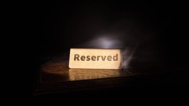 Masaya ayırtılmış tabela. Ahşap masaya bir etiket yerleştirilmiş. Karanlıkta rezervasyonu olan metal etiket. Bir restoranda rezervasyon masası. Renkli ışıklarla yaratıcı bir kavram. Seçici odak