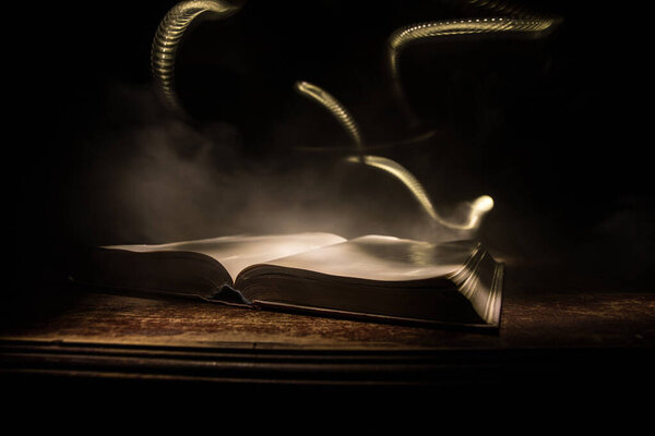 A stack of old books. Vintage book on wooden table. Magic lightning around a glowing book in the room of darkness. Selective focus