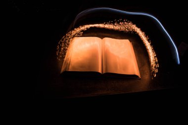 Bir yığın eski kitap. Ahşap masanın üzerinde antika bir kitap. Karanlıkta parlayan bir kitabın etrafında sihirli bir yıldırım. Seçici odak