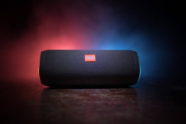 BAKU. AZERBAIJAN - 28.07.2020: JBL Flip 4 Bluetooth Hoparlörü, ahşap masaya yakın çekim, renkli ışıklar ve arka planda sis. Seçici odak