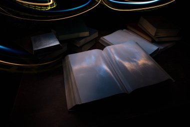 Bir yığın eski kitap. Ahşap masanın üzerinde antika bir kitap. Karanlıkta parlayan bir kitabın etrafında sihirli bir yıldırım. Seçici odak