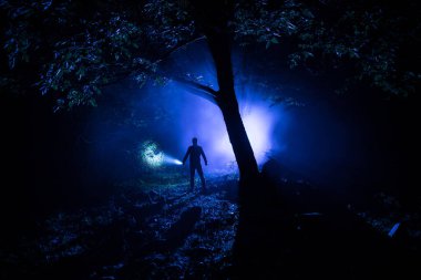 Karanlık ormanda ışıkla duran bir insan silueti. Korku Cadılar Bayramı konsepti. Gecenin karanlığında ürkütücü bir ormanda tuhaf bir siluet.