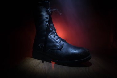 Savaş konsepti. Koyu renkli sisli bir geçmişi olan eski bir asker ayakkabısı. Yaratıcı askeri saldırganlık kavramı. Seçici odak