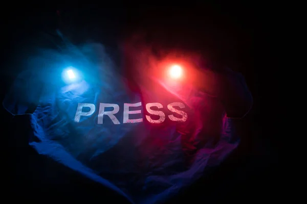 Media Journalism Global Daily News Content Concept. Blue journalist (press) vest in dark with backlight and fog. Police lights red and blue. Selective focus