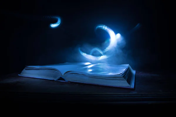 A stack of old books. Vintage book on wooden table. Magic lightning around a glowing book in the room of darkness. Selective focus