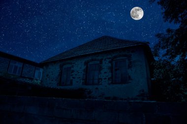 Sisli bir gecede ormanda bir hayaletin olduğu eski bir ev ya da House 'un ayın altında olduğu bir gece sahnesi. Ölü ağaç ormanındaki eski mistik bina..