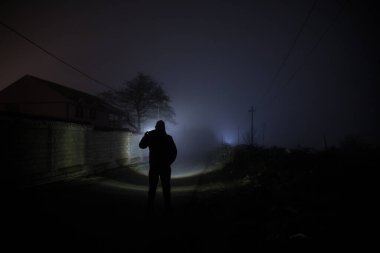 Karanlık ormanda ışıkla duran bir insan silueti. Korku Cadılar Bayramı konsepti. Karanlık ve ürkütücü bir köyde tuhaf bir siluet.