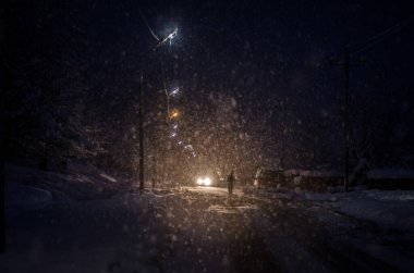 Adam, düşen karlı arka planda bir orman yolunda duruyor. Gece vakti. Kar taneleri ile bulanık