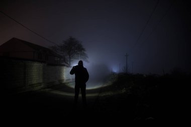 Karanlık ormanda ışıkla duran bir insan silueti. Korku Cadılar Bayramı konsepti. Karanlık ve ürkütücü bir köyde tuhaf bir siluet.