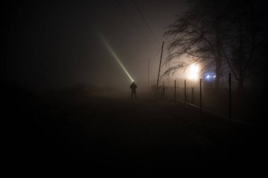 Karanlık ormanda ışıkla duran bir insan silueti. Korku Cadılar Bayramı konsepti. Karanlık ve ürkütücü bir köyde tuhaf bir siluet.