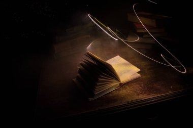 Bir yığın eski kitap. Ahşap masanın üzerinde antika bir kitap. Karanlıkta parlayan bir kitabın etrafında sihirli bir yıldırım. Seçici odak