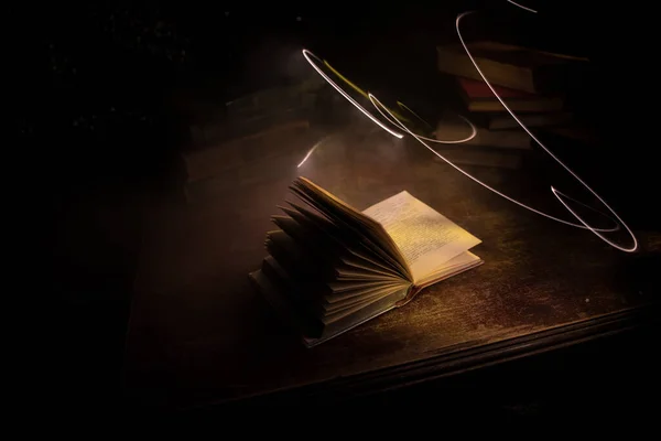A stack of old books. Vintage book on wooden table. Magic lightning around a glowing book in the room of darkness. Selective focus